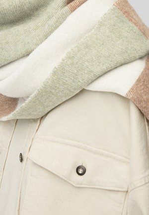 Veste en tissu crème avec poche à rabat boutonnée noire, surmontée d'une écharpe en laine aux tons doux de vert, blanc et beige.