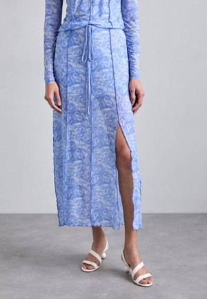 Hellblaues Kleid mit Rosendruck, durchscheinendem Stoff, langen Ärmeln, Kordelzug in der Taille und einem seitlichen Schlitz. Kombiniert mit weißen Riemchensandalen.