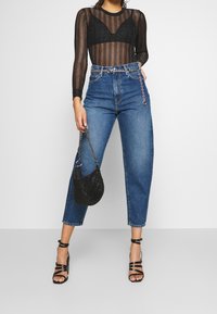 T-shirt long en voile noir à rayures verticales, jeans en denim bleu taille haute, escarpins noirs à lanières et un petit sac à main noir avec des détails en chaîne.