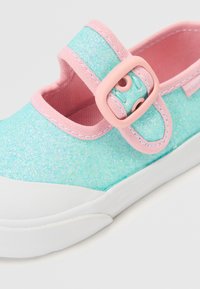 Sapato cintilante turquesa com uma correia e fivela rosa. Apresenta uma sola de borracha branca e um cabedal de tecido suave, projetado para conforto e estilo.