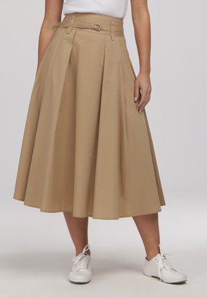 Beżowa midi spódnica w linii A z wysokim stanem i paskiem, noszona z białymi trampkami i białym topem włożonym do środka.