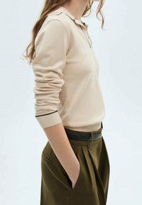 Hell-beige Langarm-Polo mit strukturiertem Kragen und dunkler Borte, kombiniert mit hoch-taillierten olivgrünen Hosen. Glatte Textur.