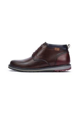 Bottines en cuir marron avec une finition lisse, un bout rond, un col sombre contrastant et une semelle en caoutchouc texturée avec des accents rouges.