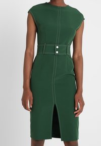 Robe verte au design ajusté, manches courtes, taille ceinturée avec deux boutons, fente avant et détails de couture contrastés.