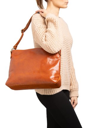 Donna che indossa un maglione lavorato a maglia beige e pantaloni neri, con una grande borsa a tracolla in pelle marrone sulla spalla destra.