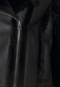 Svart läderjacka med silverfärgad dragkedja och mjuk svart fårskinnsfoder längs dragkedjan och sömmarna.