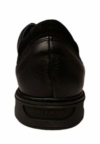 Zapato de cuero negro con un acabado suave, tacón bajo y nombre de la marca grabado en la suela. Forma redondeada con detalles de costura sutiles.