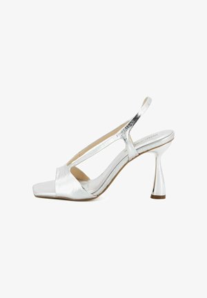 Sandalo con tacco alto slingback in metallo argento, punta aperta e tacco svasato di media altezza su sfondo bianco.