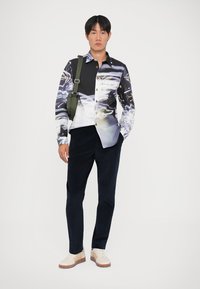 Overhemd met knopen en een abstract zwart-wit patroon, lange mouwen, contrasterende kraag, gecombineerd met donkere broek en witte sneakers.