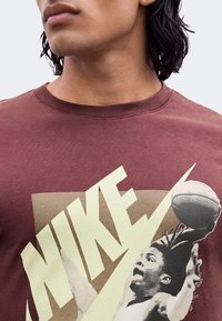 Κοντινό σε άτομο που φοράει μπλούζα Nike μπορντό με γραφικό παίκτη μπάσκετ σε vintage στυλ και μεγάλο λογότυπο Nike.