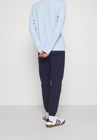 Hellblaues Sweatshirt mit gerippten Bündchen und Saum, kombiniert mit navy Jogginghosen. Weiße Sneaker mit navy und braunen Akzenten.