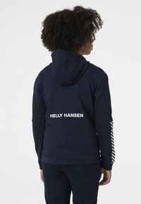Sudadera azul marino con un bolsillo tipo canguro, con un logo blanco de "HELly HANSEN" y detalles a rayas en las mangas. Tejido texturizado.