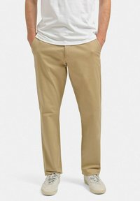 Beige chino-bukser i bomuldsmateriale, med lige ben-design, der har frontlommer og en glat overflade, parret med afslappede hvide sneakers.