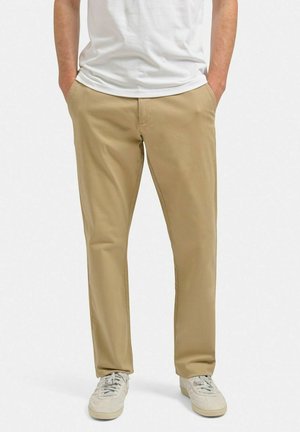 Beige chino-bukser i bomuldsmateriale, med lige ben-design, der har frontlommer og en glat overflade, parret med afslappede hvide sneakers.