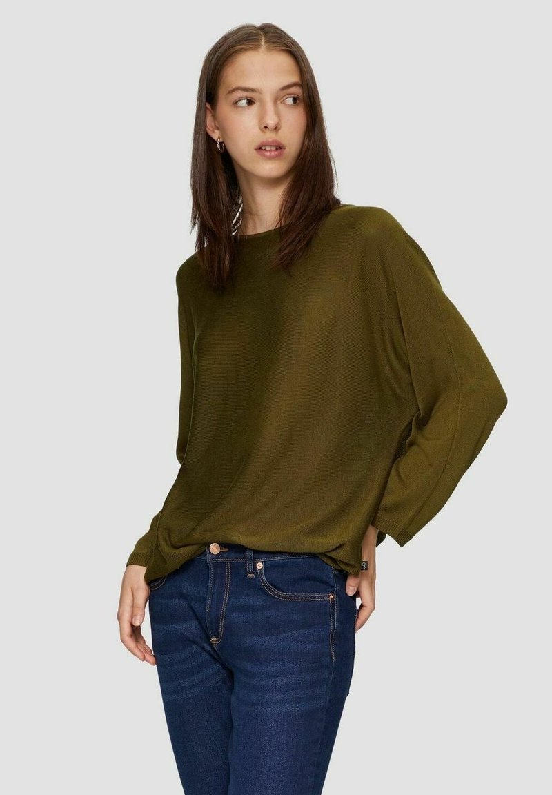 Olijfgroene, oversized shirt met lange mouwen en een ribbelstructuur. Gecombineerd met donkerblauwe jeans, met een standaard tailleband en knopen.