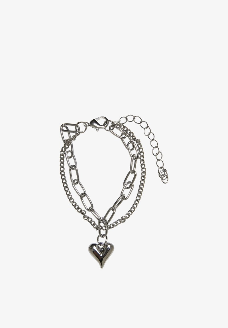 Bracelet à double chaîne en argent avec un charm en forme de cœur et un fermoir mousqueton sur fond blanc.