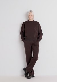 Brown matching sweatshirt and pants in a soft, textured material, featuring a relaxed fit and minimal detailing. Black sneakers complete the look.