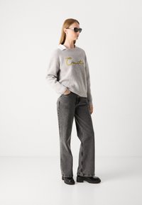 Gray knitted sweater with yellow "Craft" embroidery, paired with high-waisted gray jeans and black platform boots. Model wears black sunglasses.