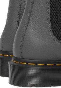 Las botines de cuero gris presentan un acabado texturizado con paneles de malla negra, costuras amarillas a lo largo de la suela y suelas exteriores de goma con perfilado.