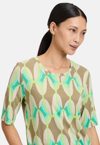 Short-sleeve top in beige with geometric green and blue patterns. Features a rounded neckline and soft, smooth texture.