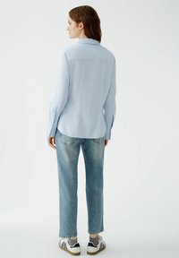 Light blue button-up shirt with a back yoke and pleats, paired with light blue straight-leg jeans and black and white sneakers.