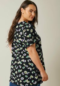 Top negro con estampado floral que presenta margaritas blancas y moradas con detalles verdes. Manga corta y corte relajado, fabricado con tejido ligero.