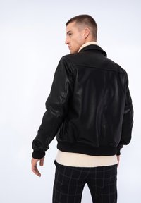Veste bomber en cuir noir avec des poignets et un ourlet côtelés, dotée d'une texture lisse et d'un design structuré. Modèle présenté de dos.