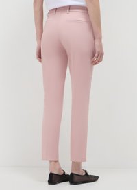 Rosa zugeschnittene Hose mit schmaler Passform, ausgestattet mit zwei Gesäßtaschen, umgeschlagenen Säumen und einer glatten Textur. Kombiniert mit schwarzen flachen Schuhen.