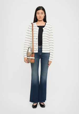 Woman wearing a white striped cardigan, black top, dark flared jeans, black flats, and carrying a beige and brown crossbody bag.