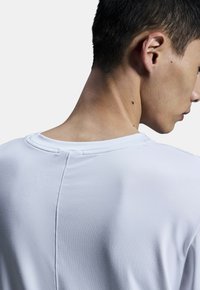 White athletic t-shirt with a smooth texture, round neckline, and visible seam detail on the back, worn by a person facing slightly away.