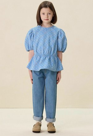 Light blue puff-sleeve top with a peplum hem, featuring a subtle pattern, paired with light blue denim jeans and beige slip-on shoes.