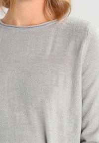 Pull gris à manches longues présentant une texture côtelée et un col rond, avec une coupe décontractée et un tissu doux.