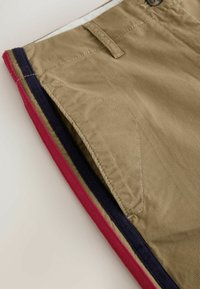 Short kaki avec poche avant, passants de ceinture et bordure latérale à rayures alternées bleu marine et rouge.
