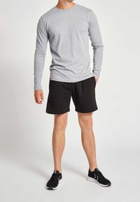 Maglietta grigia a maniche lunghe, pantaloni corti neri e scarpe sportive nere. La maglietta è semplice, i pantaloni corti hanno tasche laterali e un orlo rifinito.