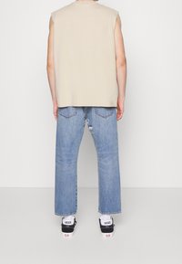 Beige ärmlös skjorta, ljusblå slitna jeans, svarta Vans sneakers. Avslappnad stil med en ledig silhuett. Enkla, moderna design detaljer.