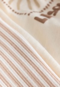 Prim-plan al unui material bej deschis și alb cu dungi, lângă un material crem cu design parțial imprimat maro.