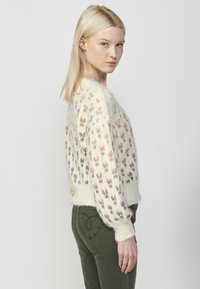 Pulover tricotat în crem cu un design modelat ce prezintă fluturi multicolori. Material gros, texturat; manșete și tiv cu tiv în relief.
