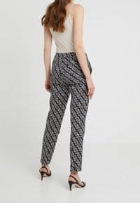 Spodnie w kolorze granatowym z kremowym wzorem w zygzaki, dopasowany fason i zwężane nogawki. Materiał wydaje się lekki. Noszone z butami na wysokim obcasie.