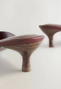 Sandali alti in pelle bordeaux con tacco in legno a campana e una delicata punta arrotondata. Presentano cuciture visibili lungo il bordo.