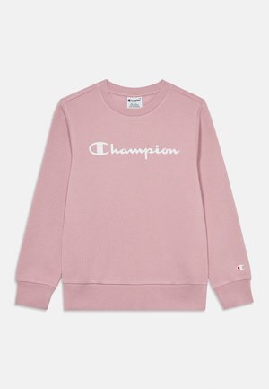 Jasnoróżowa bluza Champion z długimi rękawami z białym logo na piersi i małym logo na lewym mankiecie.