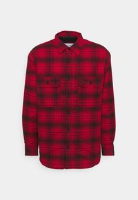 Red and black plaid button-up shirt with long sleeves, two front pockets, and black buttons. Textured fabric with a classic check pattern.