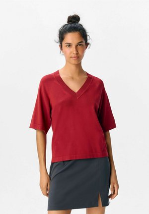 Top rosso a maniche corte con scollatura a V, dal taglio rilassato, realizzato in un materiale morbido, abbinato a una gonna grigia scura con uno spacco laterale.