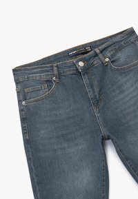 Schlanke Jeans in dunkelblauer Denim mit kontrastierenden orangen Nähten, Vorderstaschen, einer Metallknopf-Verschluss und einem Etikett mit der Aufschrift W32 L32.
