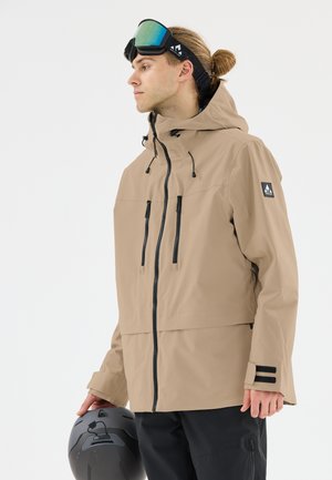 Beige vattentät jacka med huva, med svarta dragkedjor och detaljer. Slät textur, två framlommar och justerbara ärmslut.