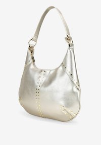 Bolso de cuero plateado metálico con acentos de tachuelas doradas, de forma curva y con una sola correa para el hombro, que cuenta con un cierre de cremallera para mayor seguridad.
