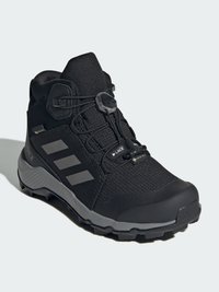 Black hiking boot featuring a textured fabric upper, lace toggle closure, rubber sole, and three gray stripes on the side.