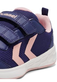 Lila Sportschuh mit pinken Akzenten, ausgestattet mit einem Obermaterial aus Mesh und einer geschwungenen weißen Sohle. Das Design umfasst Klettverschlüsse und Logodetails.