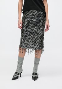 Črna midi krilo s sequin okraski in resastim robom, dopolnjeno s sivimi nogavicami do kolen in čevlji z visoko peto z zaponkami na konicah.