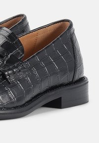 Μαύρα δερμάτινα μοκασίνια με σχέδιο κροκόδειλου, στρογγυλεμένη μύτη, μικρό τακούνι μπλοκ και λείο φινίρισμα. Εσωτερική επένδυση χωρίς ορατά διακοσμητικά.