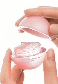 Contenant sphérique rose contenant un masque pour les lèvres gelée translucide. Le couvercle transparent révèle la texture en gel, avec un texte minimal sur le côté.